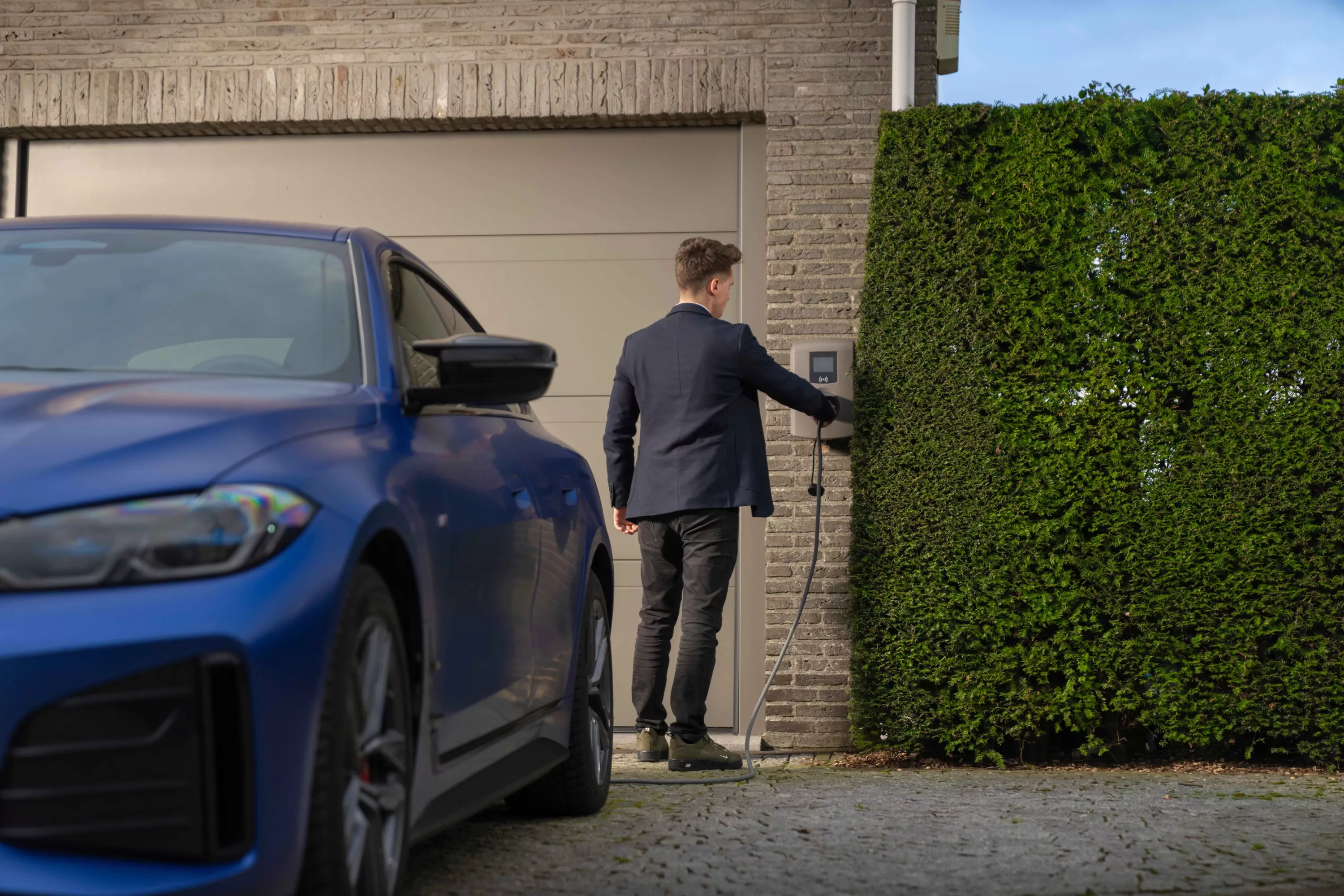 Man sluit een elektrische auto aan op een laadpaal aan huis.